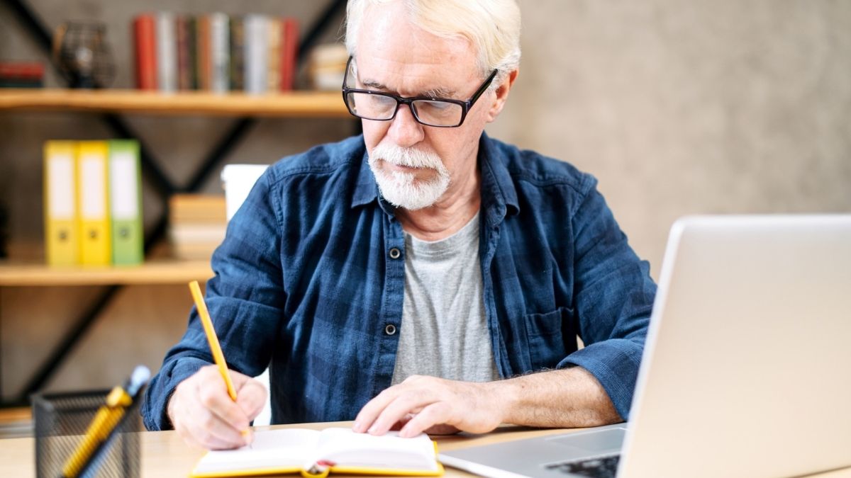 man at a computer writing in a notebook