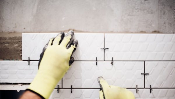 person installing tile wearing gloves in a bathroom