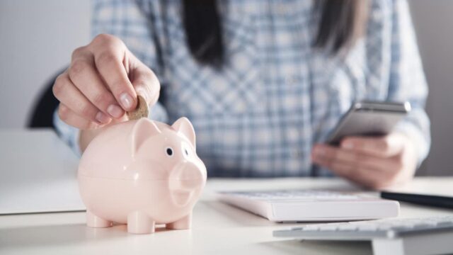 woman with phone putting money in piggy bank